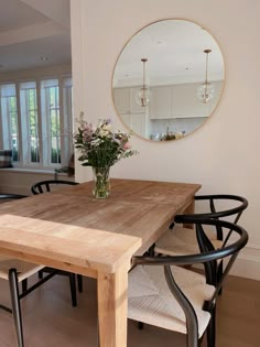 a wooden table with chairs around it in front of a round mirror on the wall