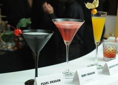 three different types of cocktails sitting on a table with people in the back ground