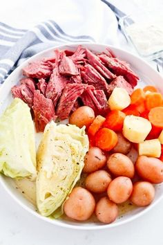 a white plate topped with meat, potatoes and carrots next to lettuce