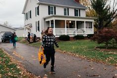 a woman is walking down the street in front of a white house with green shutters