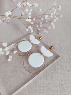 three white circular earrings sitting on top of a table next to a branch with flowers