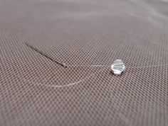 a piece of wire sitting on top of a bed next to a needle and thread