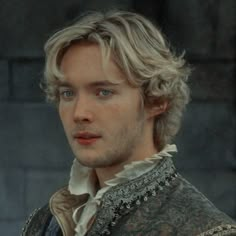 a man with blonde hair and blue eyes in a medieval costume looking at the camera