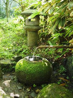 a water fountain in the middle of a garden with moss growing on it's sides