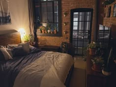 a bedroom with brick walls and plants on the window sill, bed in foreground