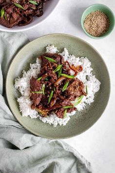 two plates filled with meat and rice on top of a white table cloth next to a bowl of seasoning