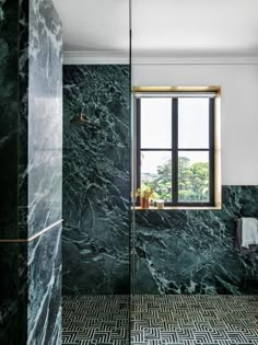 a bathroom with green marble walls and flooring, along with a window in the corner