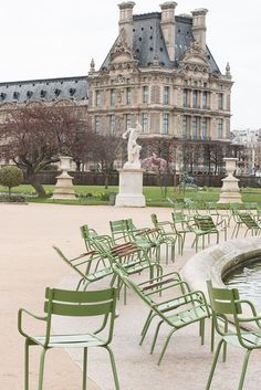 there are many green chairs in front of the fountain