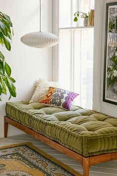 a green daybed sitting in front of a window next to a potted plant