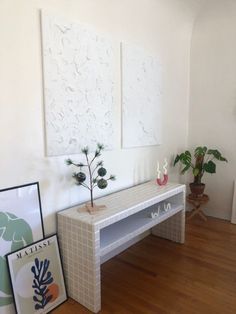 there is a white table in the room with pictures on the wall and a potted plant next to it