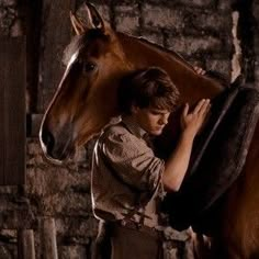 a young boy is standing next to a horse in an old barn with his back turned