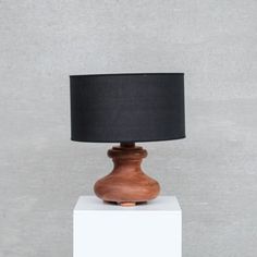 a small wooden table lamp on top of a white block with a black shade over it