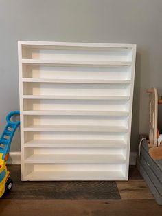 a white book shelf sitting on top of a wooden floor next to a toy car