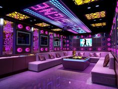 a room with couches, tables and lights on the ceiling is lit up in purple