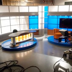 the television studio is set up with blue and orange chairs, two large tv screens, and an entertainment center