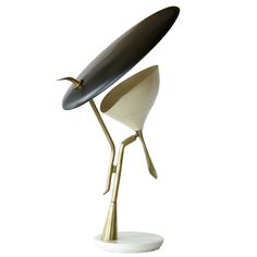 a white table lamp with a black and gold shade on it's head, in the shape of a bird