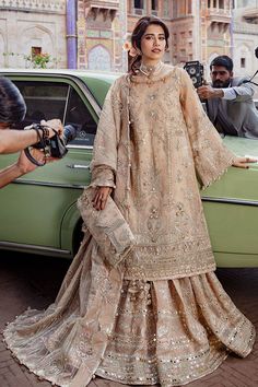 a woman standing in front of a green car wearing a dress and holding a camera