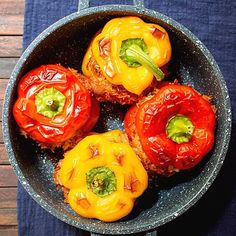 four stuffed bell peppers in a bowl on a wooden table with a blue place mat