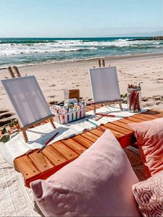 an easel on the beach with paintings and pillows