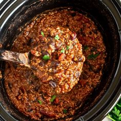 a crock pot filled with chili and beans, topped with a wooden ladle