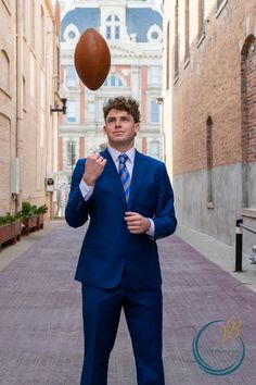 a man in a blue suit and tie is throwing a football into the air with his right hand