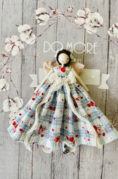 the doll is wearing a dress with cherries on it, and has a sign that says do more