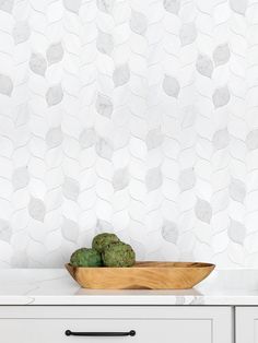 a wooden bowl filled with green vegetables on top of a counter next to a white wall