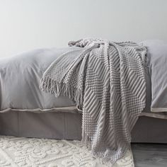 a bed with a gray comforter on top of it next to a white rug