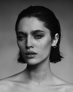 a black and white photo of a woman's face with earrings on her head