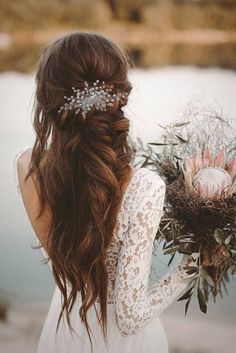 a woman with long hair holding a bouquet of flowers in her hand and looking at the water