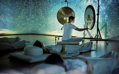 a man sitting on the floor in front of a mirror with two gongs behind him