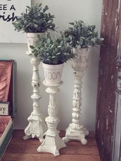 two white vases with plants on them sitting on a wooden shelf next to a book