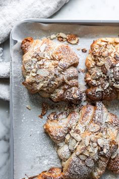 four pastries on a tray covered in powdered sugar and almonds, ready to be eaten