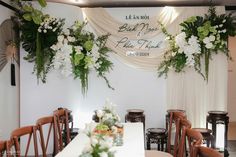 a white table topped with lots of flowers and greenery next to a wall hanging from the ceiling