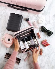 a woman is packing her travel bag with makeup and other personal care items on the table