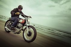 a man riding on the back of a motorcycle down a beach