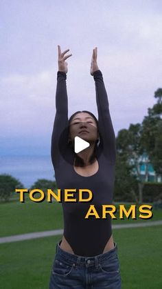 a woman standing on top of a lush green field holding her hands up in the air