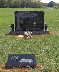 a grave in the middle of a field with flowers on it and a plaque next to it