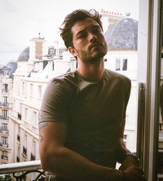 a man sitting on top of a metal bench next to a window with buildings in the background