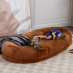 a young boy sleeping on top of a brown bean bag chair next to a cat