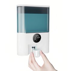 a person is holding a cup in front of a water dispenser with thermometer on it