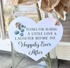 a white heart shaped sign with flowers in it sitting on a table next to a window