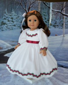 the doll is wearing a white dress with red trims and a bow in her hair