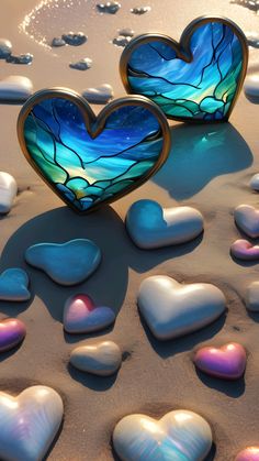 two heart shaped glass pieces sitting on top of a sandy beach next to hearts in the sand