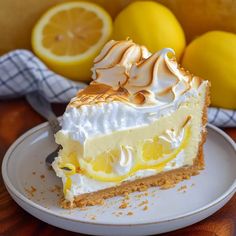 a slice of lemon meringue pie on a plate with two lemons in the background