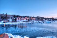 an icy lake with houses on the shore and trees in the background at sunset or dawn