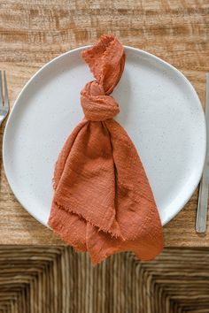 an orange napkin on a white plate with silverware