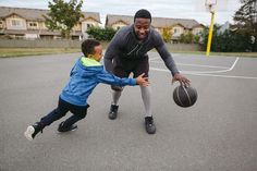 a man and boy playing basketball on an asphalt court with houses in the back ground