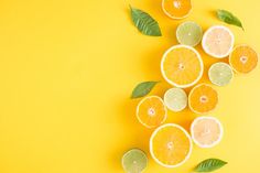 oranges and limes cut in half with leaves on yellow background, top view