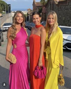 three beautiful women standing next to each other in long dresses and holding purses on the street